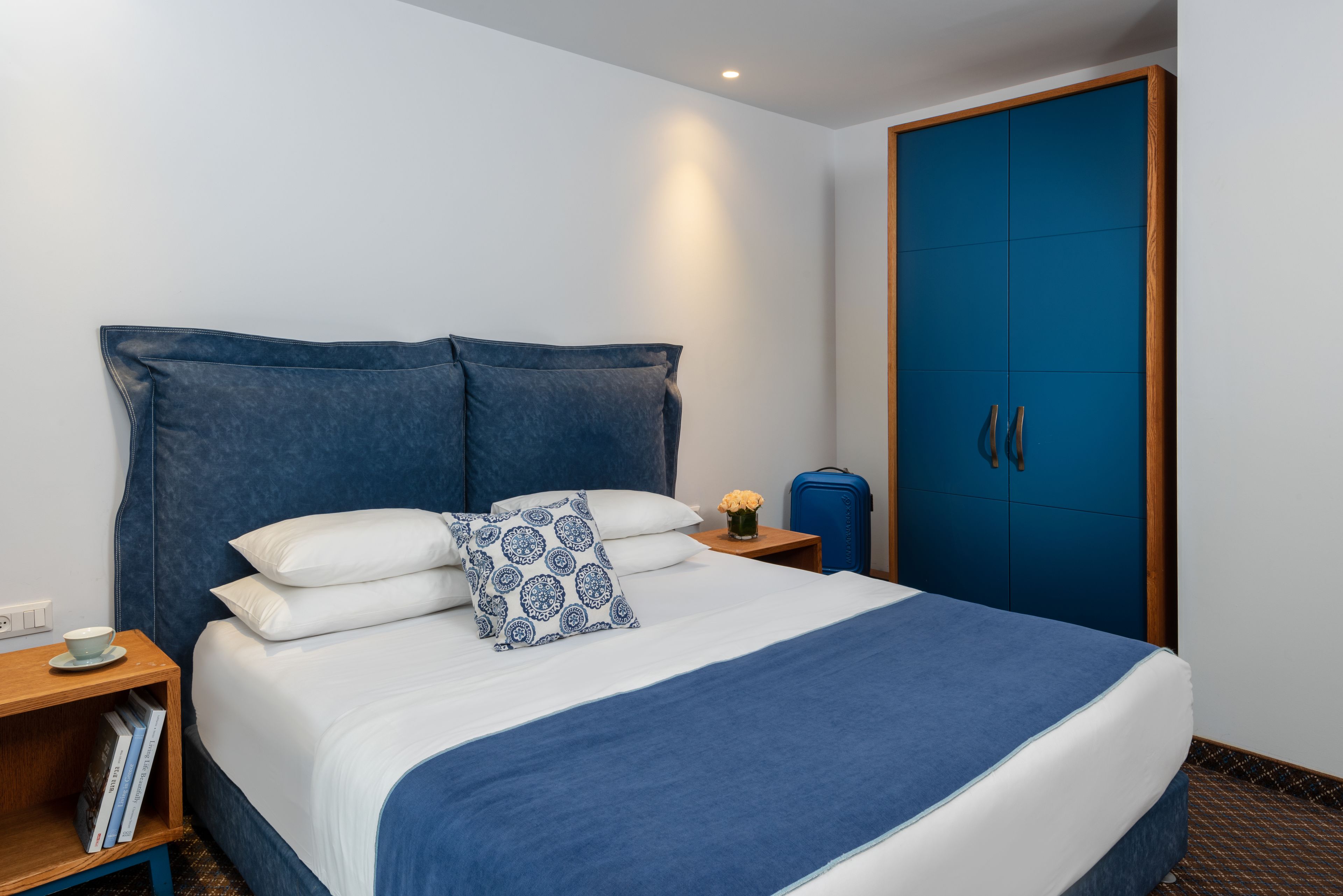 A neatly made bed with a blue and white duvet, a patterned pillow, and a bedside table with a cup and a book.