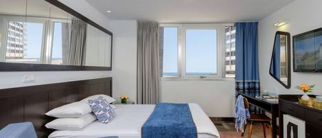 Habitación de hotel con cama, escritorio, silla, cómoda y una ventana grande con cortinas.