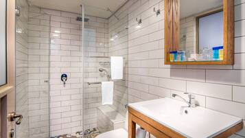 Un baño moderno con ducha de vidrio, lavamanos blanco y tocador de madera.