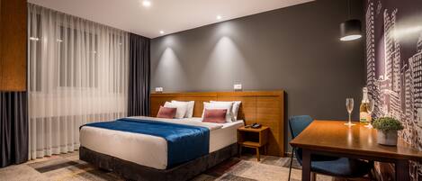 Una habitación de hotel con una cama grande, un cabecero de madera, una mesita con una silla y una pared con un mural de un paisaje urbano.