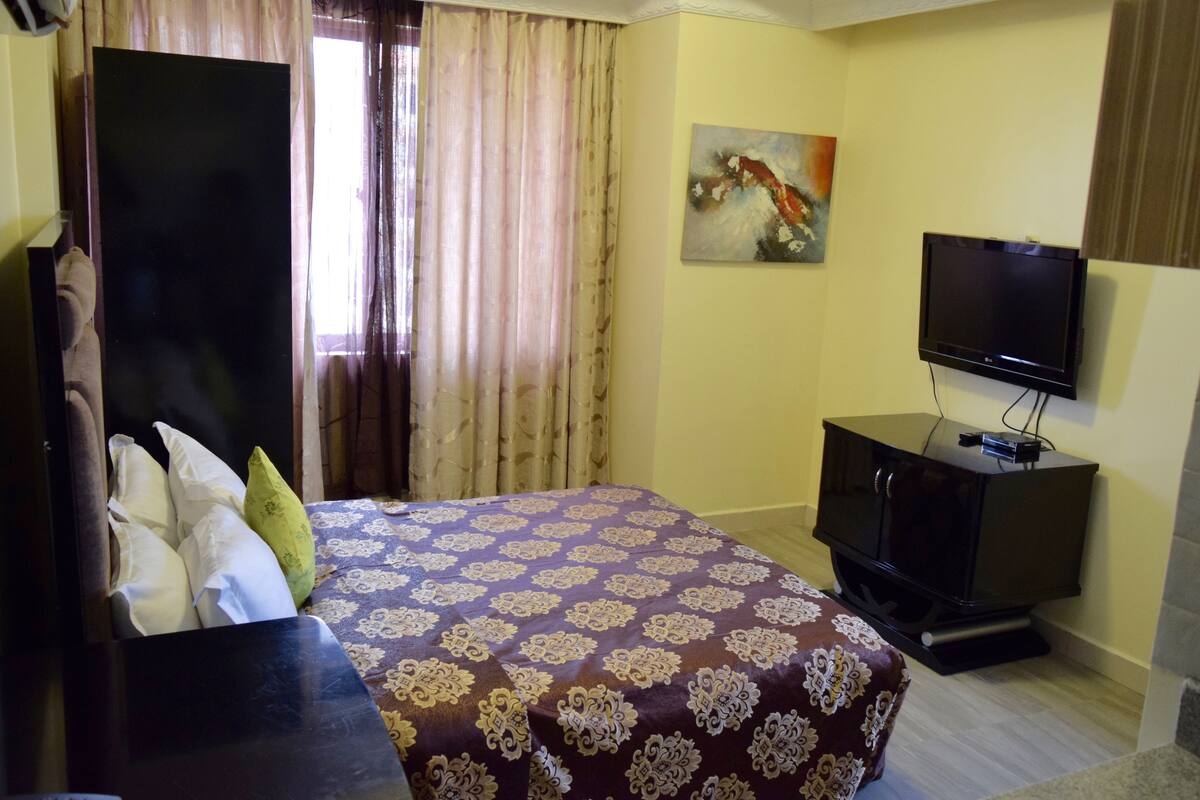 A hotel room with a bed, a television, and a painting on the wall.