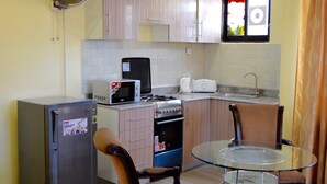 A compact kitchen with a refrigerator, microwave, toaster, and sink. There are two chairs and a small round table. - New Avon Apartments (Dar es Salaam)
