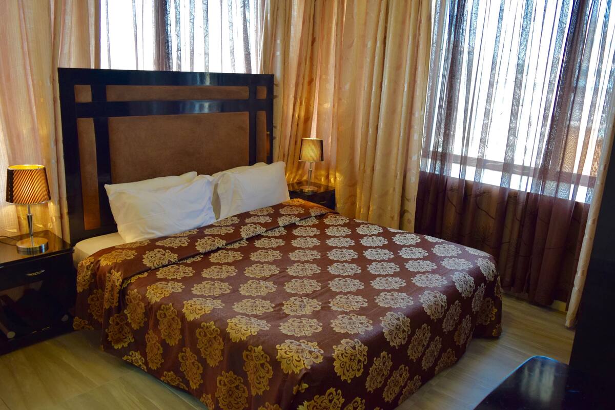 A neatly made bed with a patterned bedspread, a bedside lamp, and curtains.