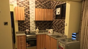 A compact kitchen with wooden cabinets, a built-in oven, a sink, and a refrigerator. - New Avon Apartments (Dar es Salaam)