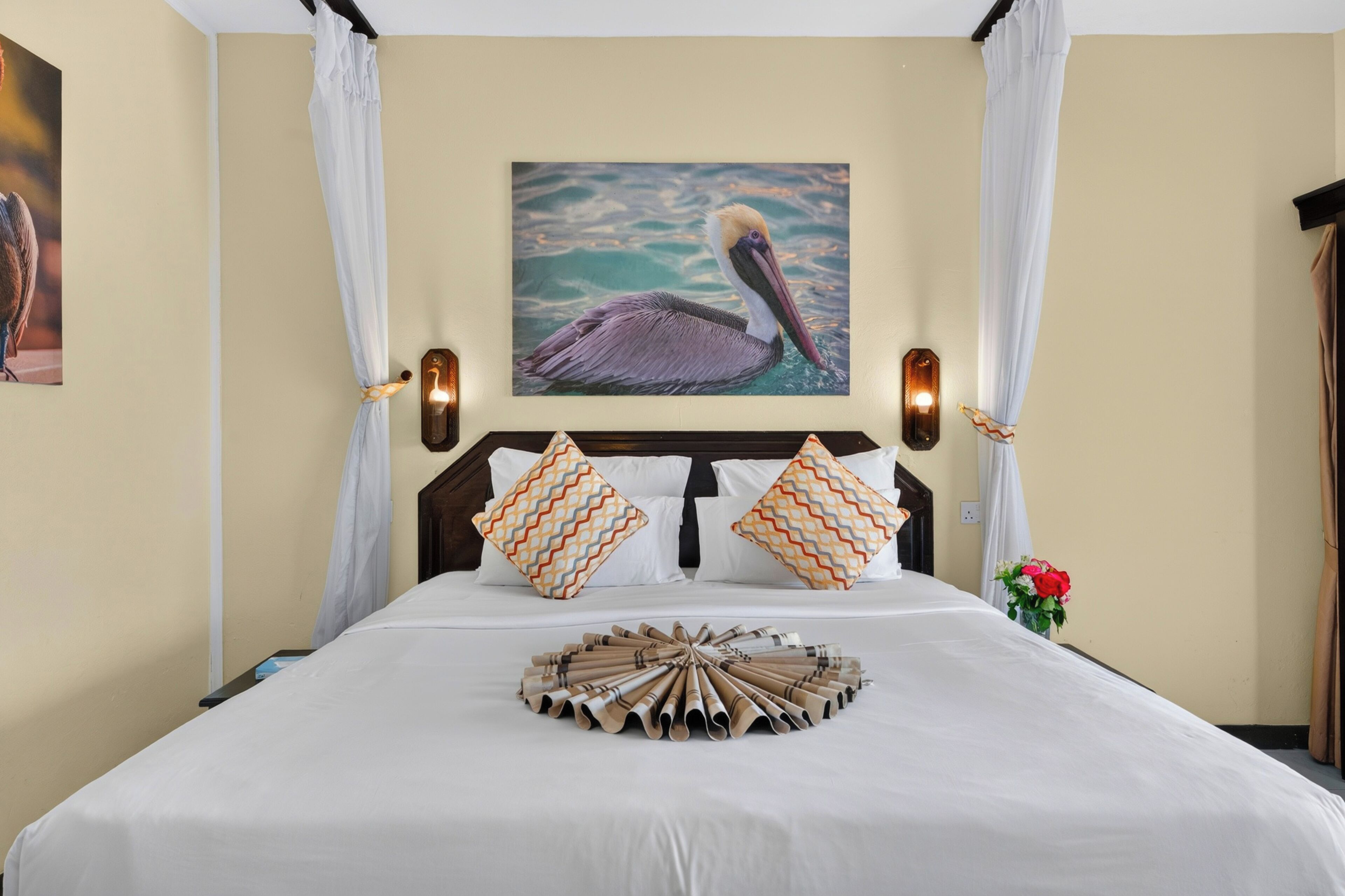A hotel room with a bed, a painting of a pelican, and a decorative wooden tray.