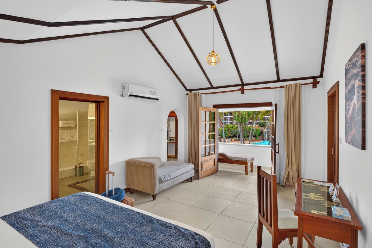 Une chambre d’hôtel équipée d’un lit, d’un canapé, d’une petite table, d’une chaise, d’un climatiseur et offrant une vue sur une piscine.