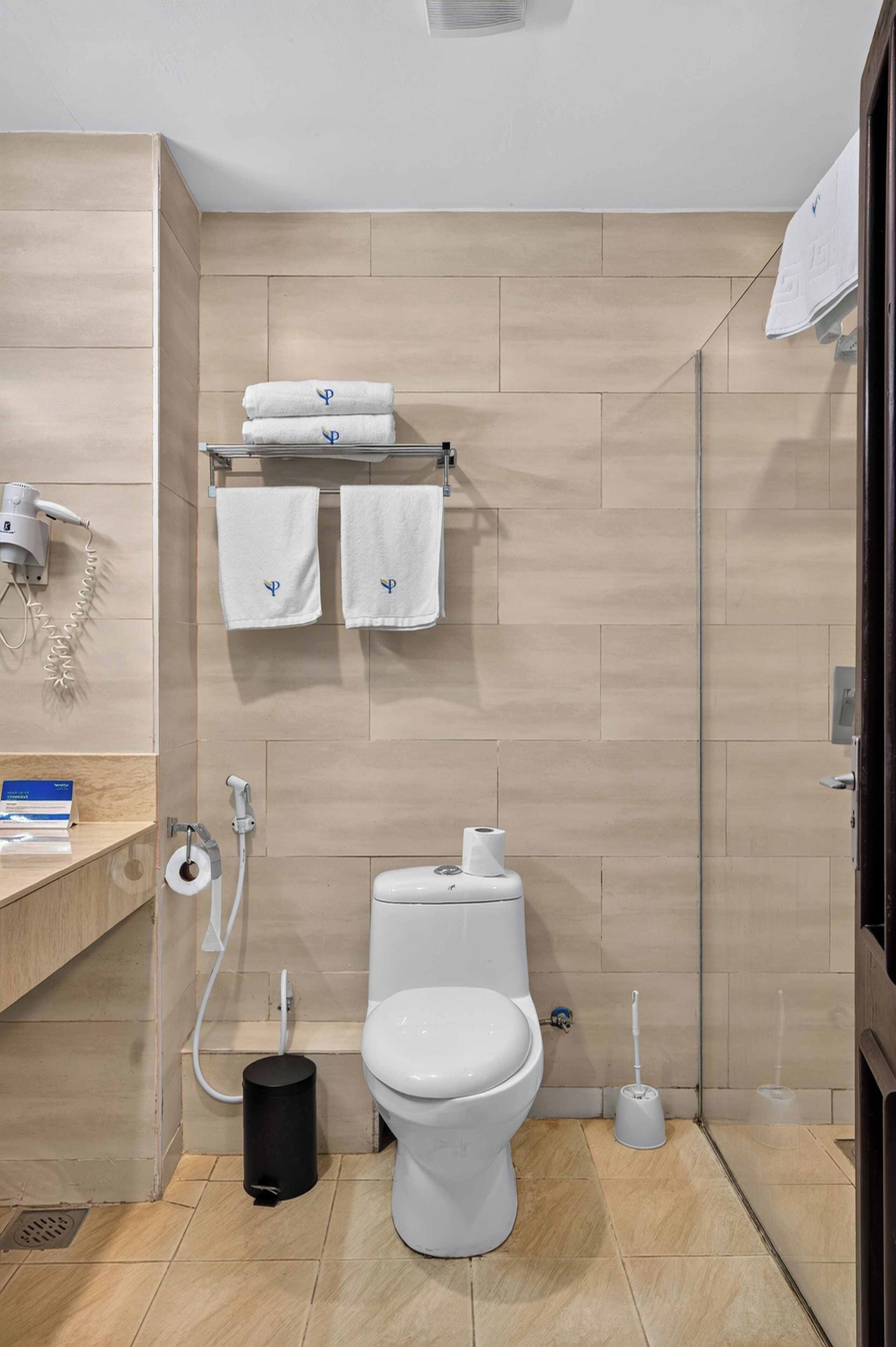 A modern bathroom with a toilet, a hand dryer, a towel rack with towels, and a toilet paper holder.