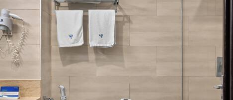 A modern bathroom with a toilet, a hand dryer, a towel rack with towels, and a toilet paper holder.