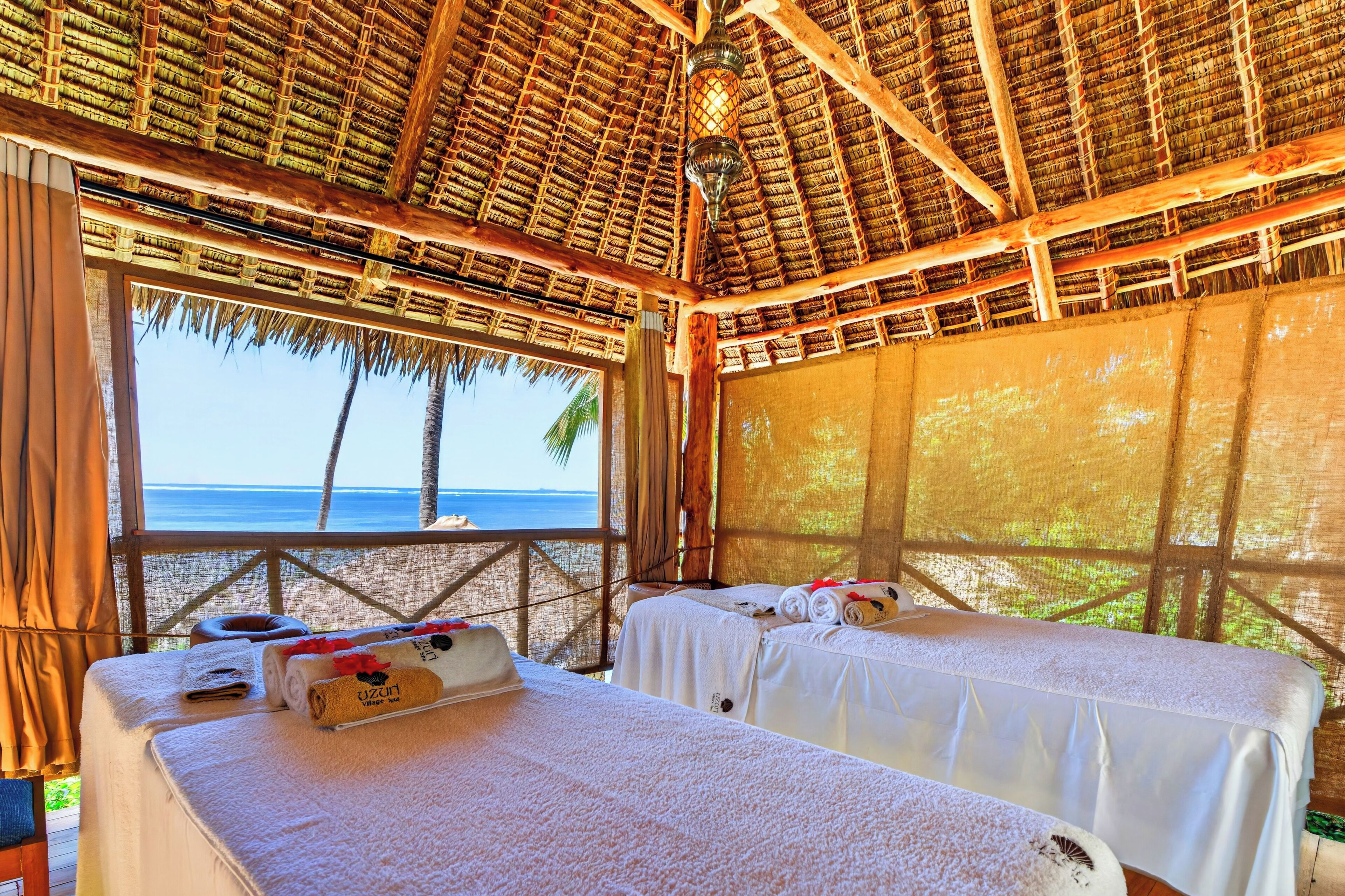 Ein Zimmer am Strand mit zwei Betten, einem Reetdach und Blick auf das Meer.