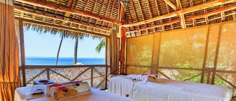 A beachside room with two beds, a thatched roof, and a view of the sea.