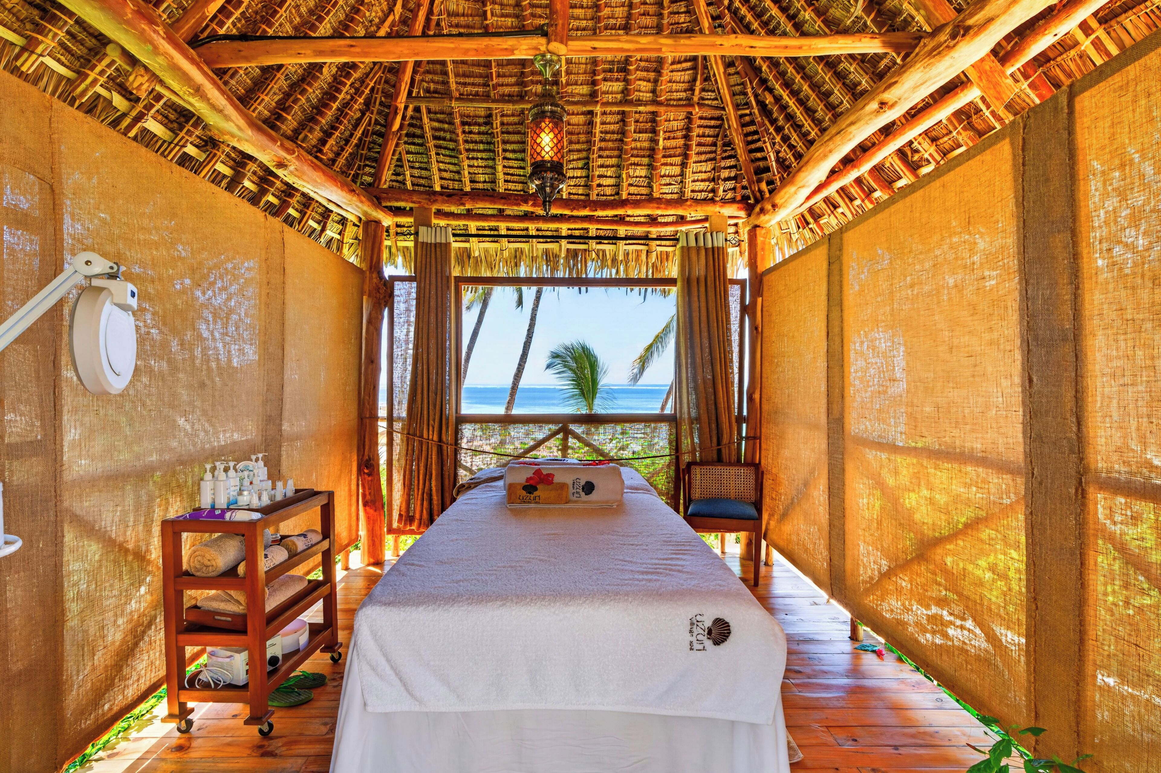 Una habitación con cama, una mesa de masajes, un estante con artículos de aseo y vista al océano.