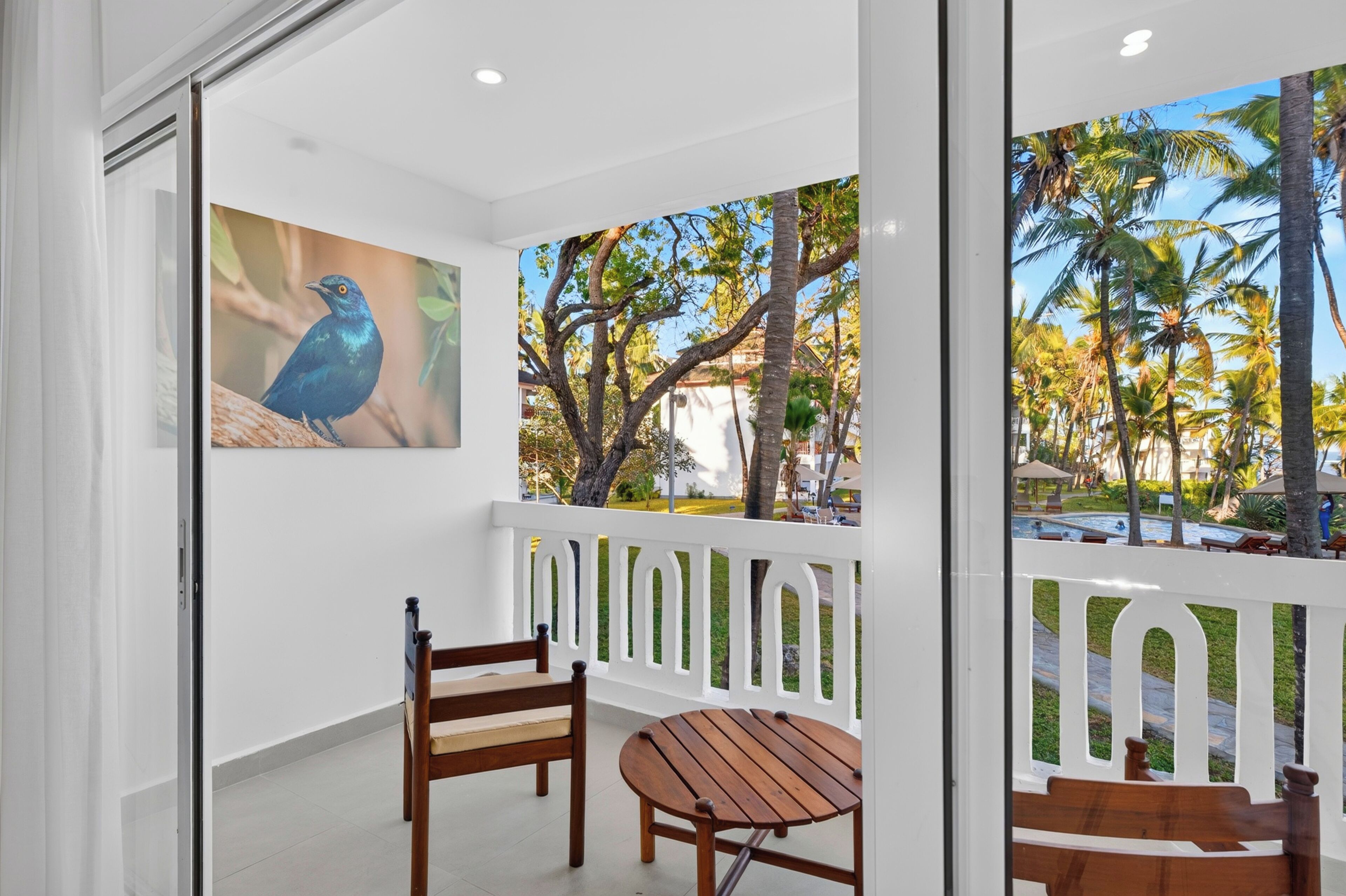 Varanda com mesa e cadeiras de madeira, guarda-corpo branco e uma pintura de um pássaro.