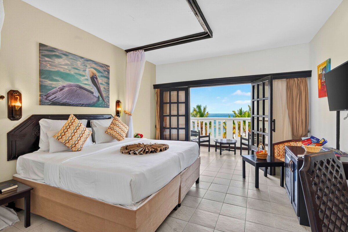 Une chambre d’hôtel avec un lit, un tableau représentant un pélican, un balcon avec vue et une télévision.