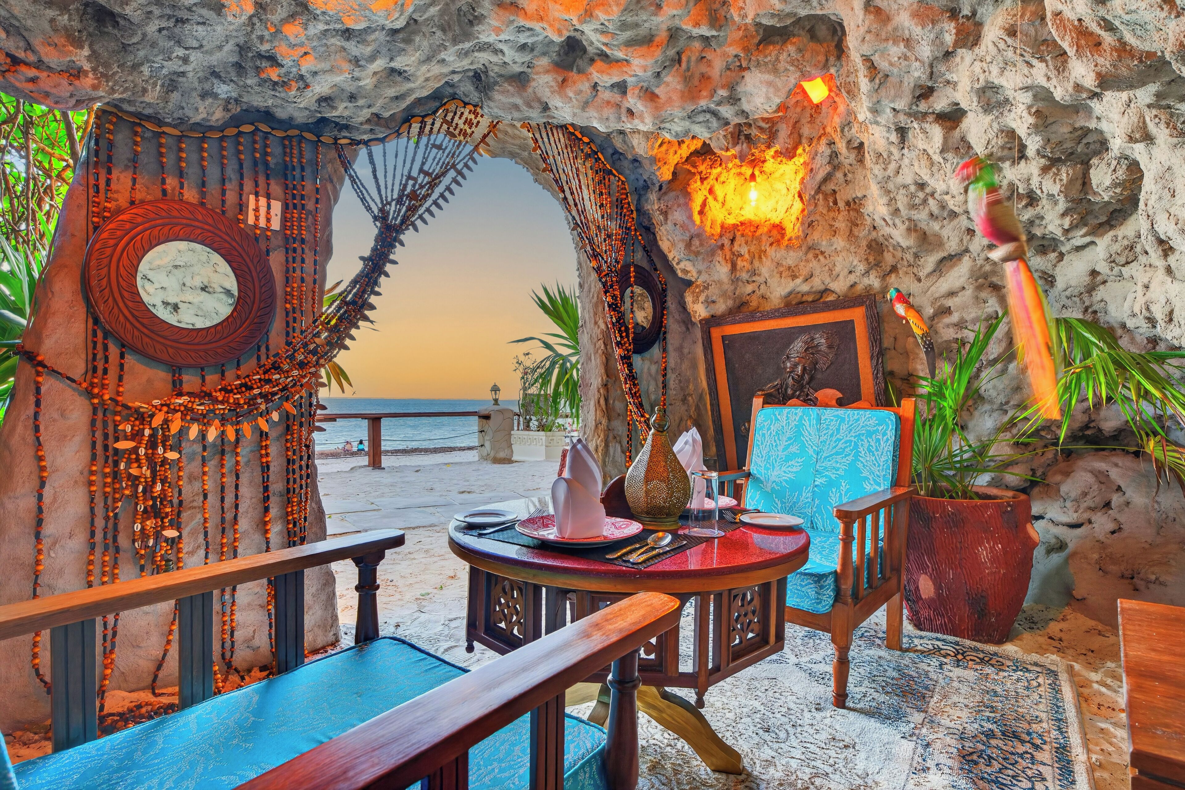 Uma área de refeições com vista para o mar, com uma mesa posta, pratos, talheres e um abajur decorativo.