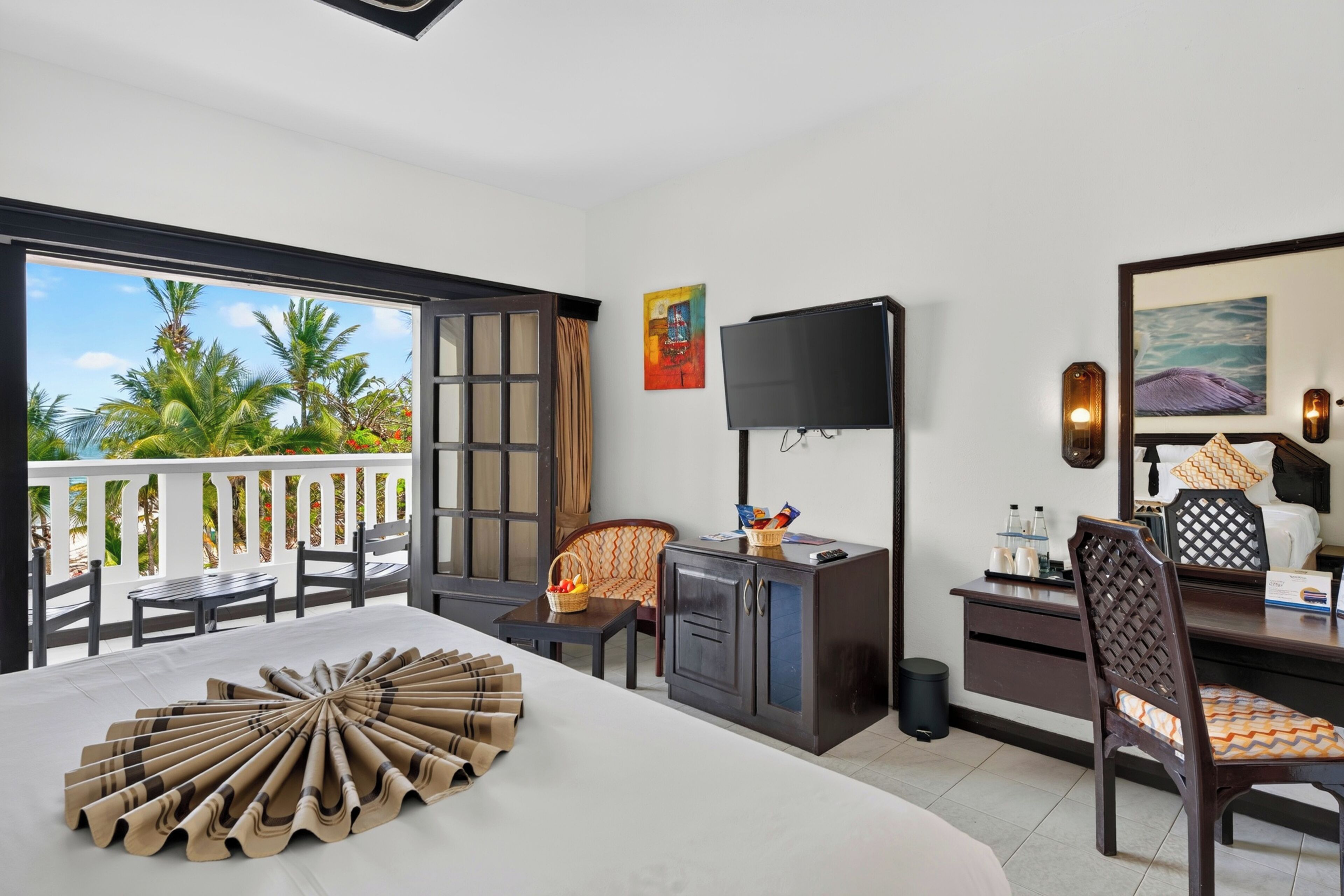 A hotel room with a balcony, a TV, a desk with a chair, and a bed.