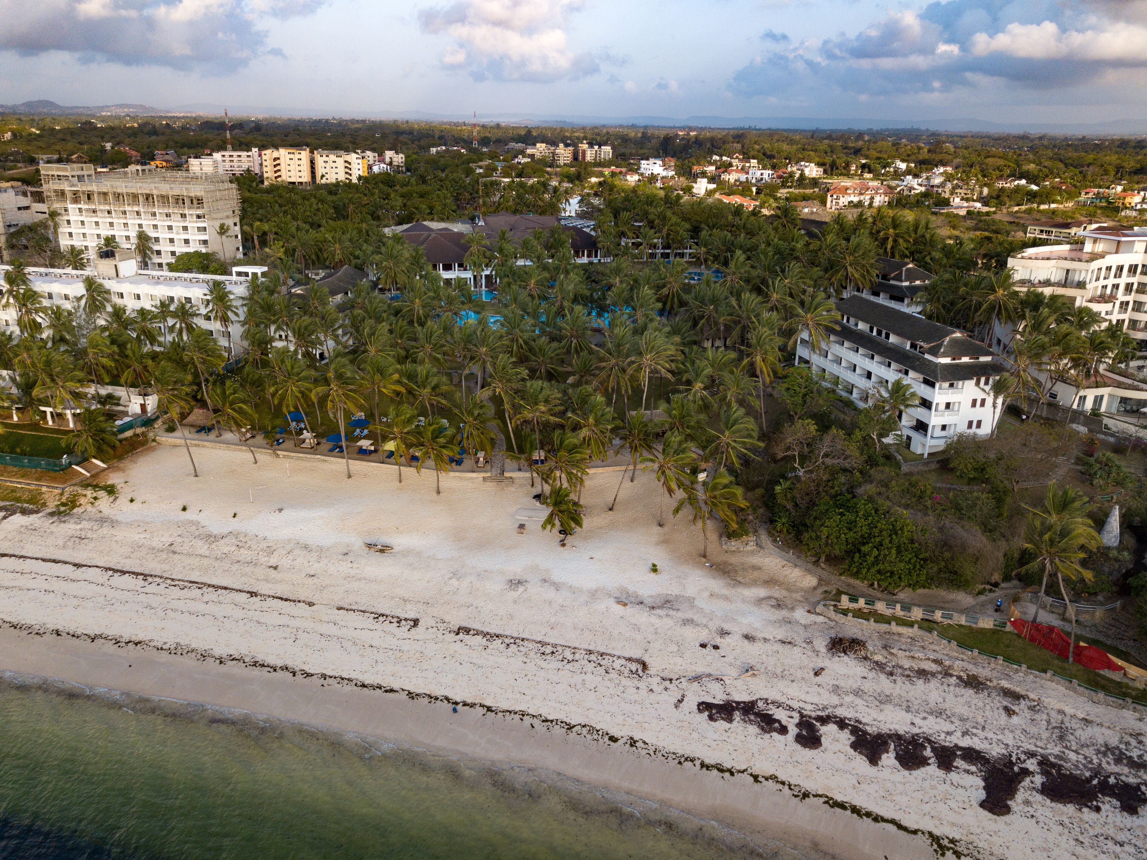 An aerial view of a coastal area with a beach, palm trees, and buildings.