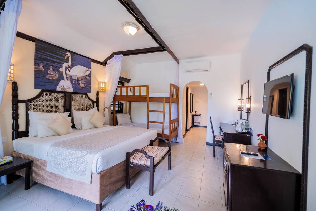 A bedroom with a large bed, a wooden bench, a desk, a TV, and a painting of swans.