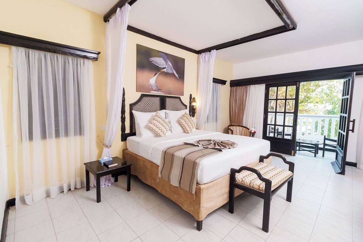 A bedroom with a large bed, a nightstand, a chair, and a view of the outdoors.