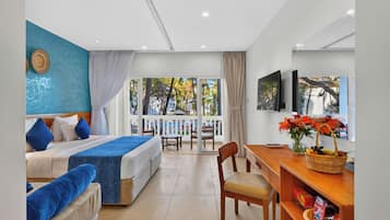 Habitación de hotel con cama, escritorio, silla, televisor y balcón con vista a palmeras.