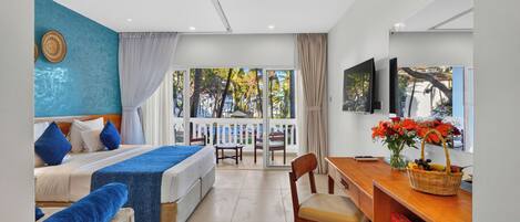 Habitación de hotel con cama, escritorio, silla, televisor y balcón con vista a palmeras.