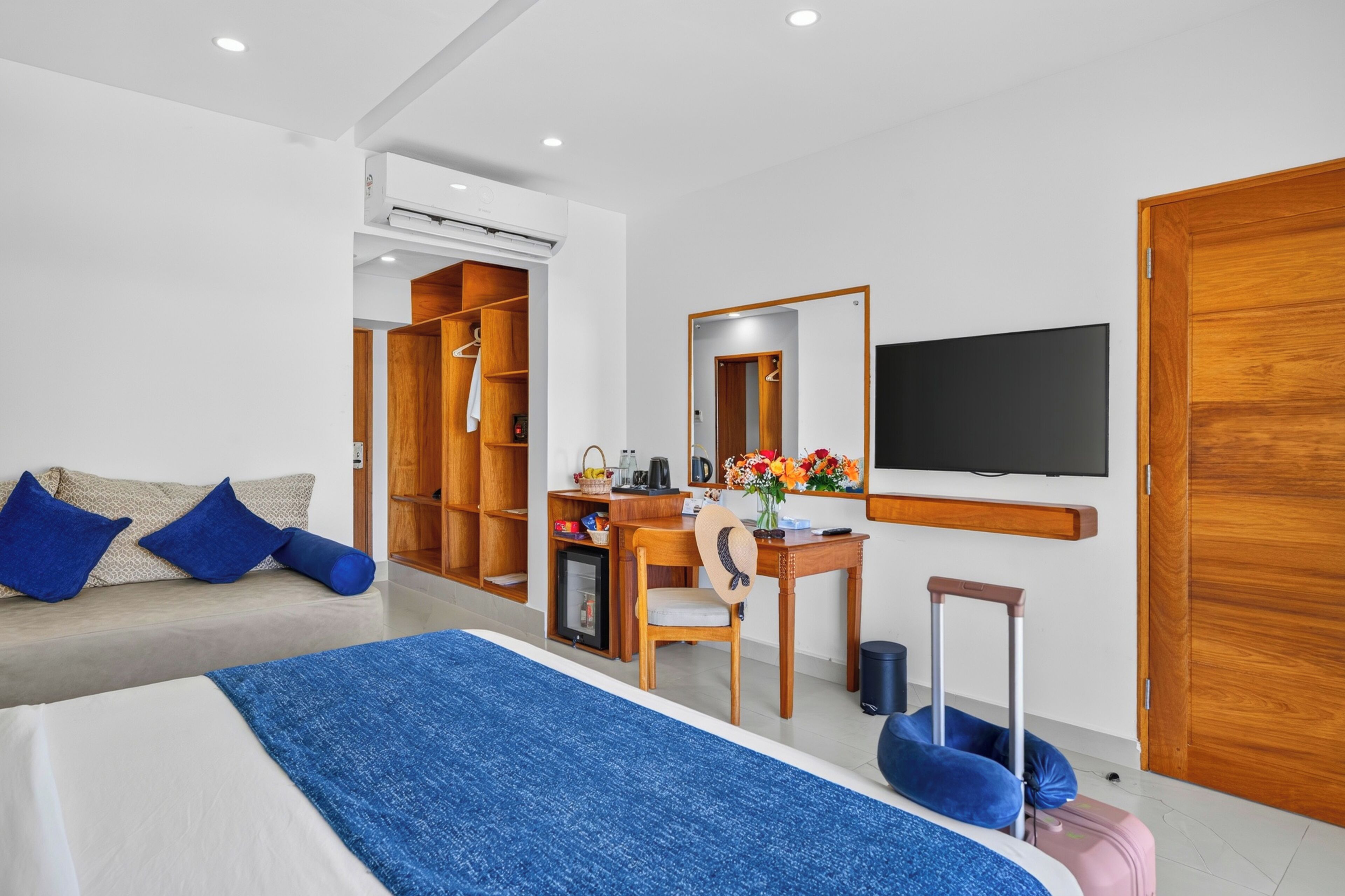 A hotel room with a bed, a desk, a chair, a TV, a wardrobe, and a small fridge.