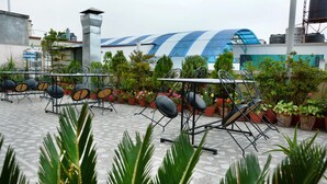 Outdoor seating with metal chairs and tables, surrounded by potted plants and a building with a blue and white striped roof. - Kathmandu Eco Hotel (Kathmandu)