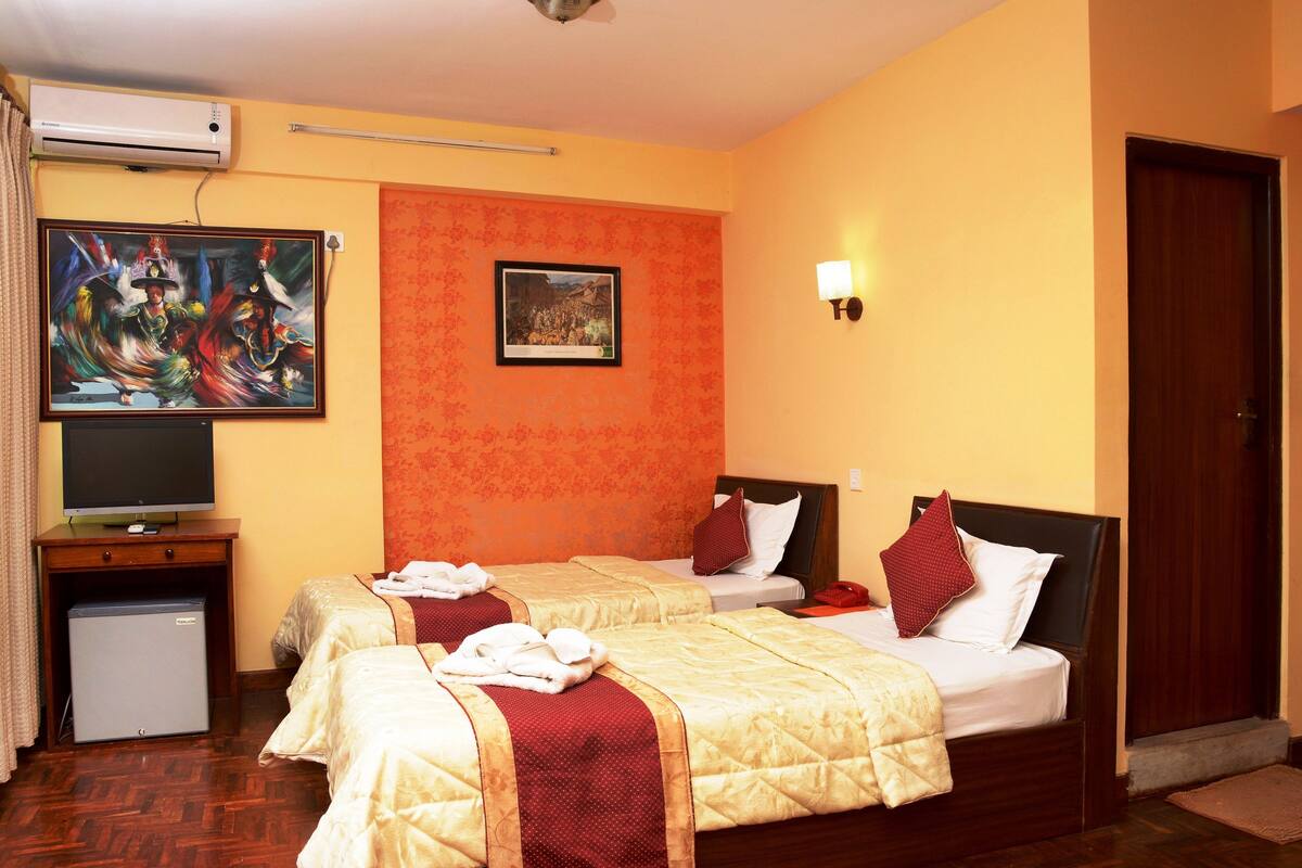 A hotel room with two beds, a TV, a small fridge, and a painting on the wall.