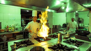 A professional kitchen with chefs, a large stove with flames, and various cooking utensils. - Kathmandu Eco Hotel (Kathmandu)