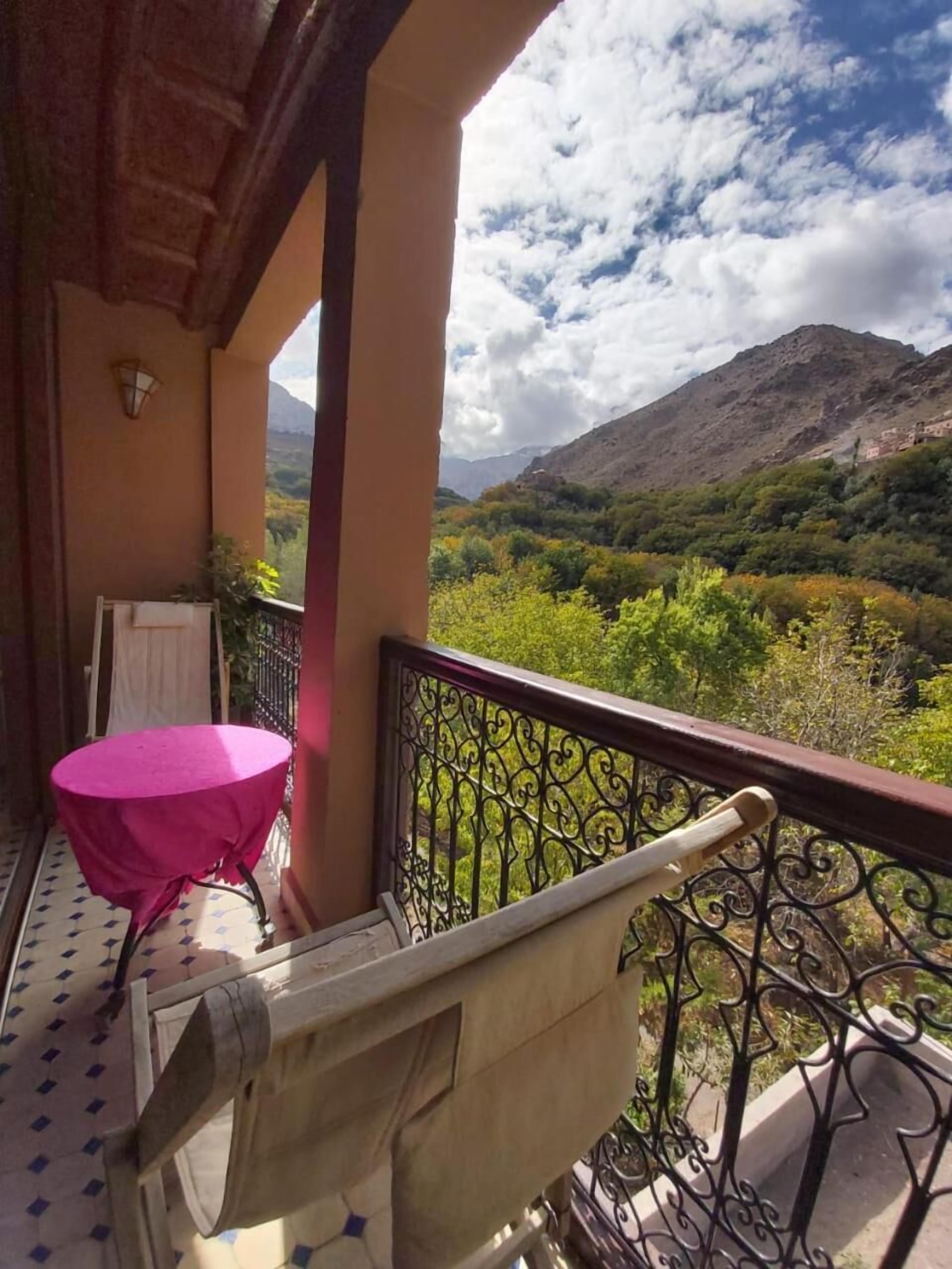 A balcony with a table and chair, a view of a mountainous landscape, and a clear sky.