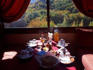 A breakfast setup with a table set for two, featuring plates, bowls, cups, and a basket of bread.