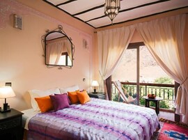 Un dormitorio con cama, mesita de noche, espejo y balcón con mesa y sillas.