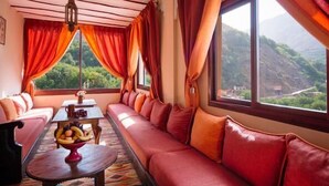 Um quarto aconchegante com sofá, mesa com frutas e vista para uma paisagem montanhosa.