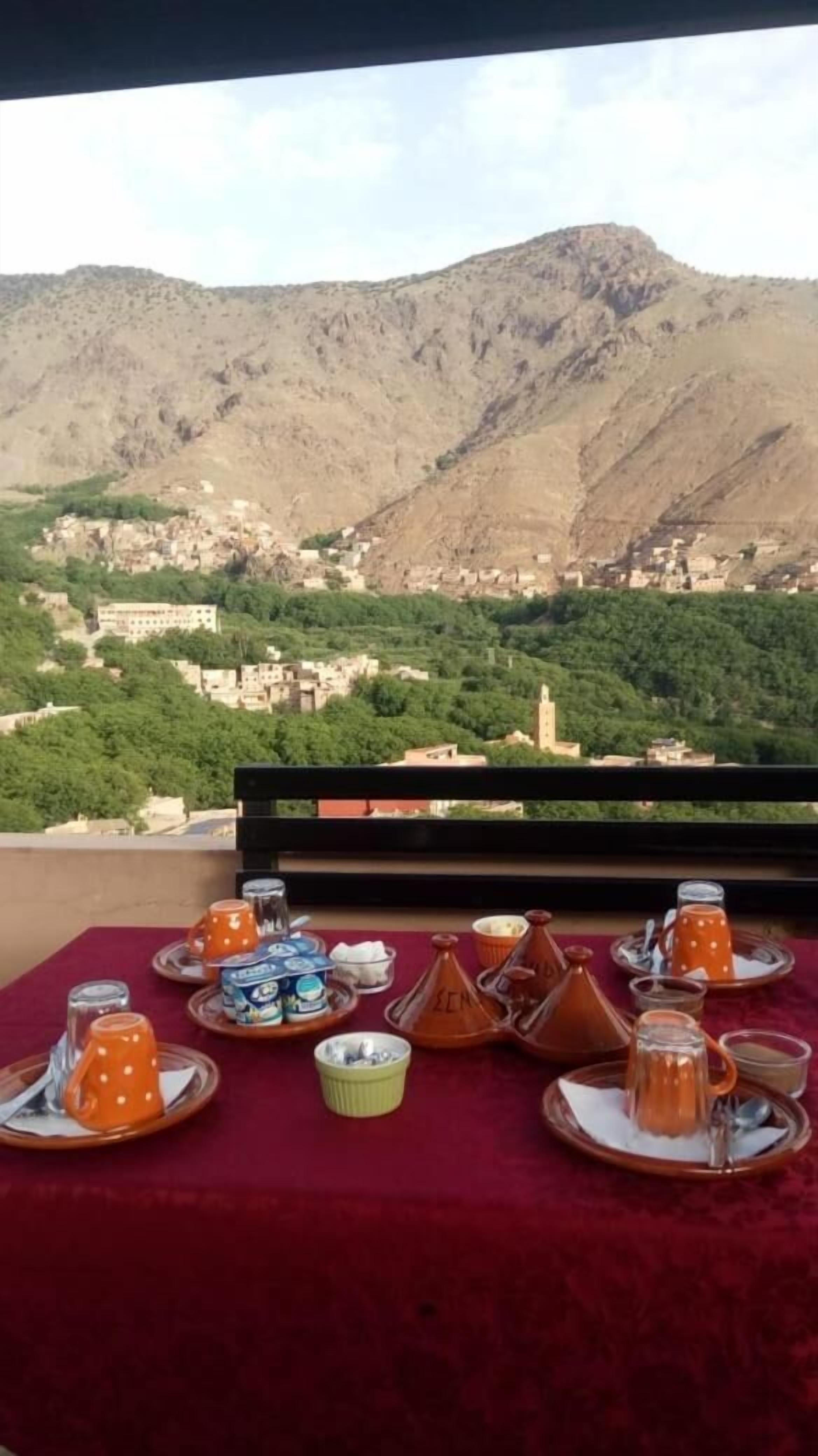 A table set with traditional Moroccan tea and snacks, overlooking a mountainous landscape with a village below.