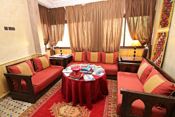 A cozy room with a red sofa set, a round table with magazines, and a patterned rug. - Riad Atlas Toubkal (Asni)