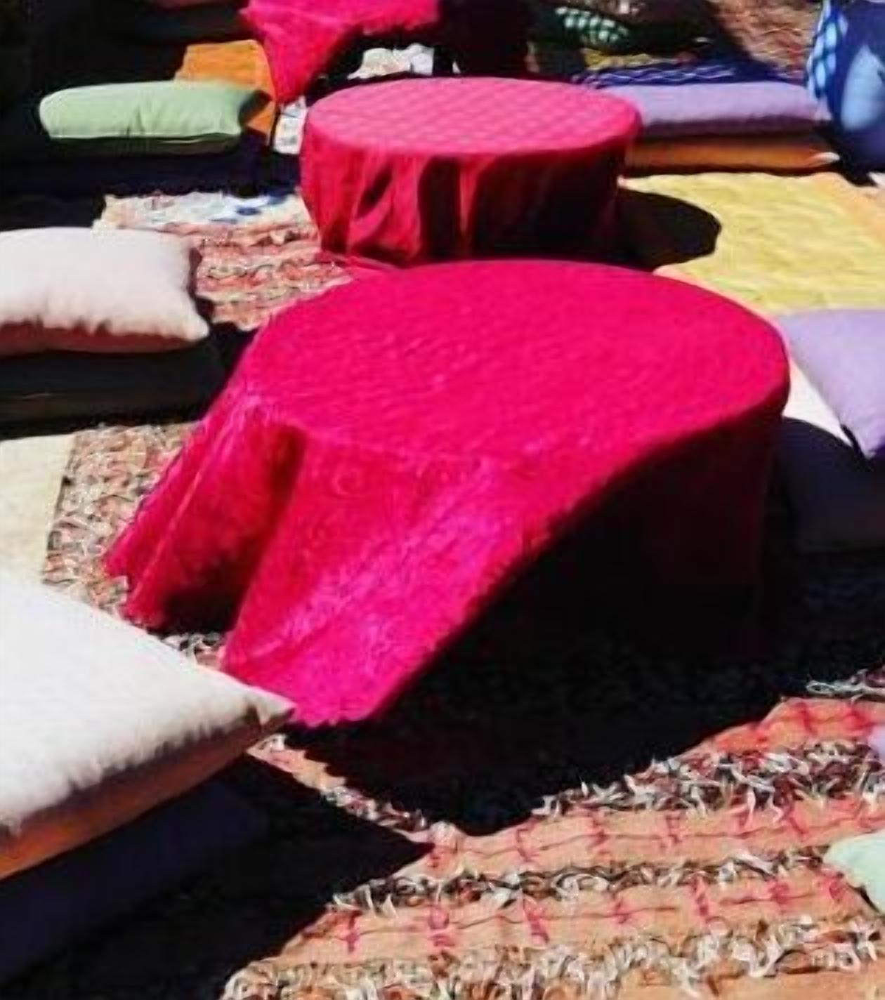 A seating area with round tables covered in red cloths, surrounded by cushions.