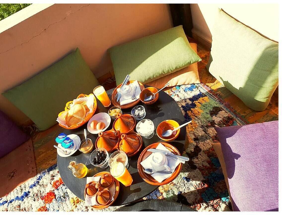 Una mesa redonda con diversos alimentos para el desayuno, como pan, huevos y bebidas, sobre una alfombra estampada al aire libre.