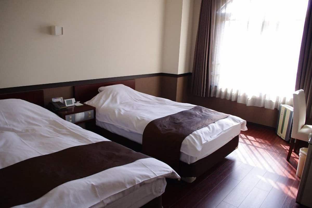 A hotel room with two beds, a nightstand, a lamp, and a window with curtains.