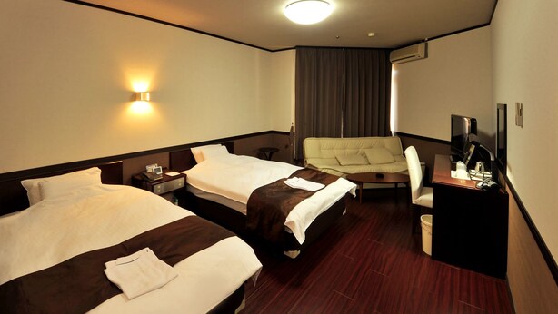 A hotel room with two beds, a sofa, a desk with a TV, and a window with curtains. - Hotel Saint Paul Nagasaki (Nagasaki)