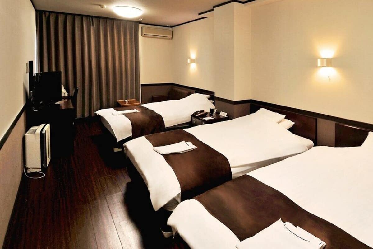 A hotel room with three beds, a TV, and a desk.