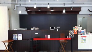 A reception desk with a computer, a telephone, and informational posters. There are two wooden chairs and a small table in front of the desk. - Hotel Saint Paul Nagasaki (Nagasaki)