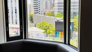 A room with a large window offering a view of a cityscape, including modern buildings and a parking area. - CYPRESS HOTEL Nagoya-eki Mae (Nagoya)