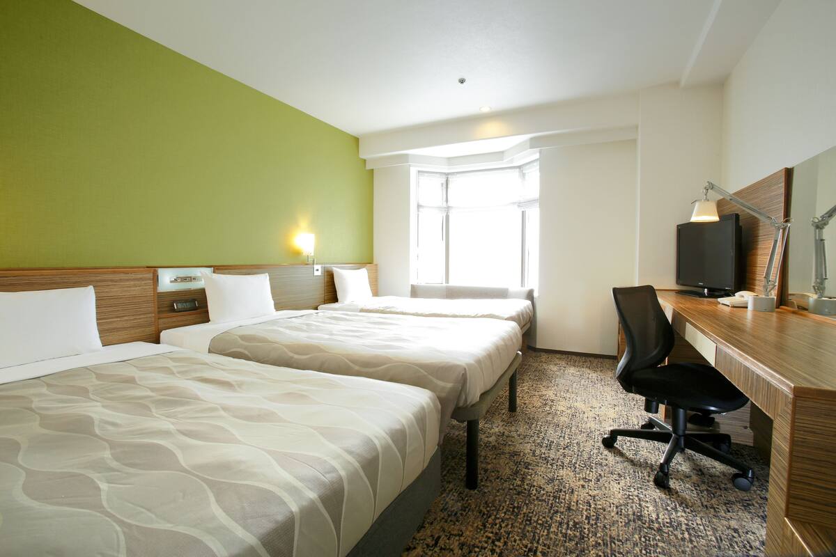 A hotel room with two beds, a desk, a chair, a television, and a window with curtains.