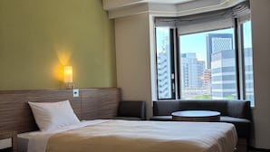 A hotel room with a large bed, a smaller bed, a sofa, a round table, and a view of tall buildings. - CYPRESS HOTEL Nagoya-eki Mae (Nagoya)