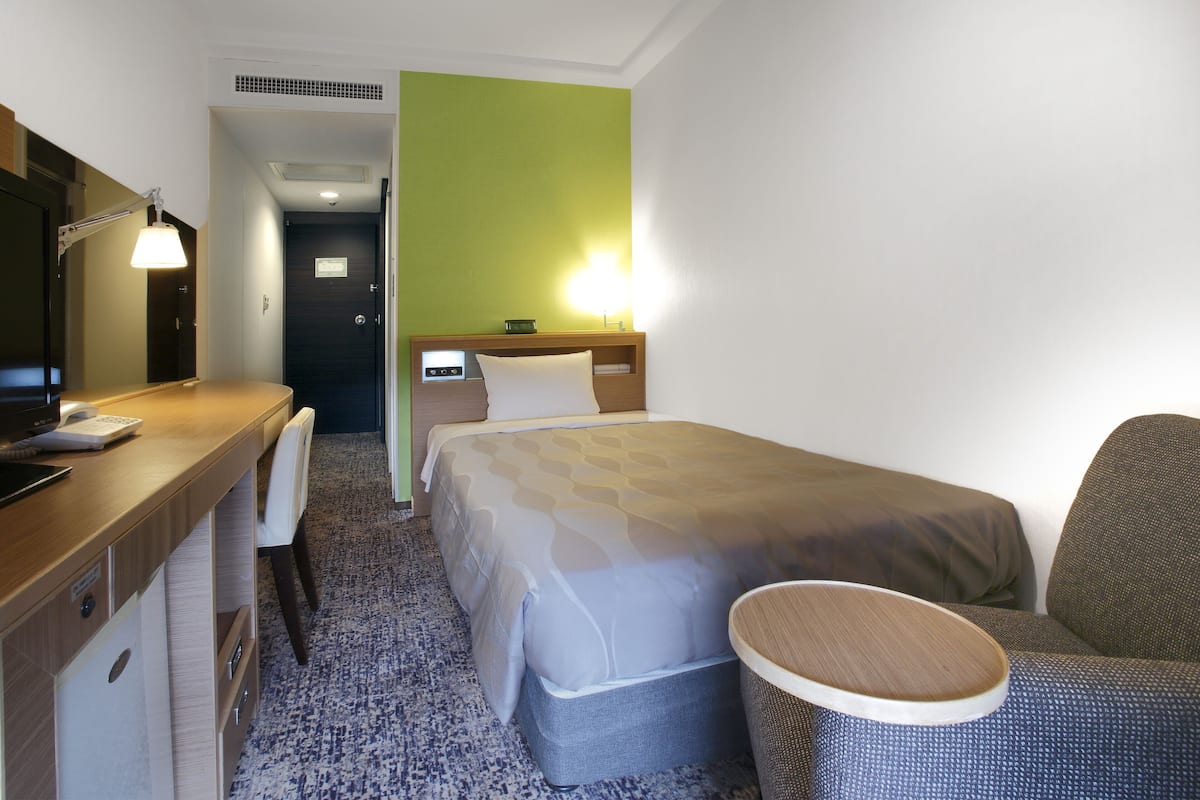 A hotel room with a bed, a desk with a computer, a chair, and a small round table.