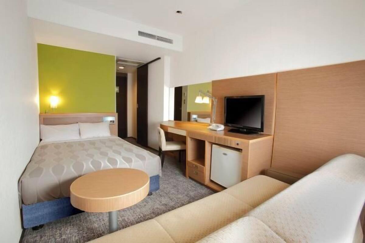 A hotel room with a bed, a desk, a television, a small table, and a sofa.