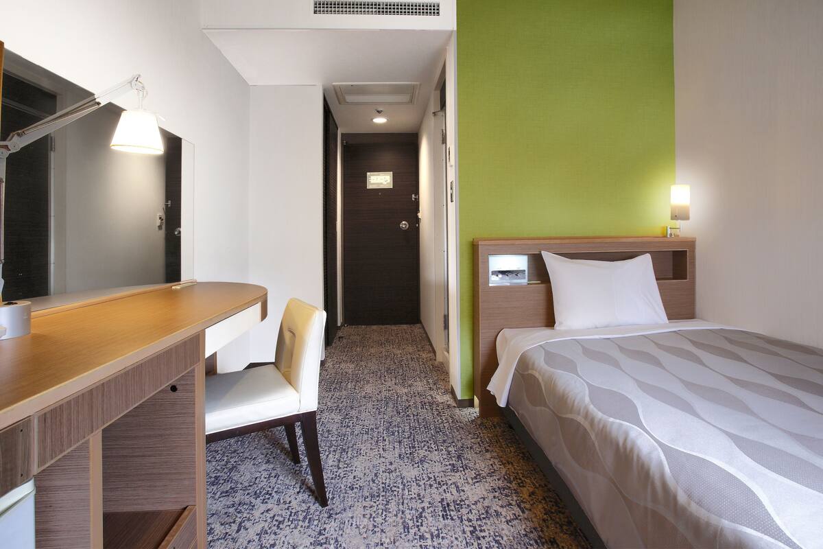 A hotel room with a desk, chair, bed, and a green accent wall.