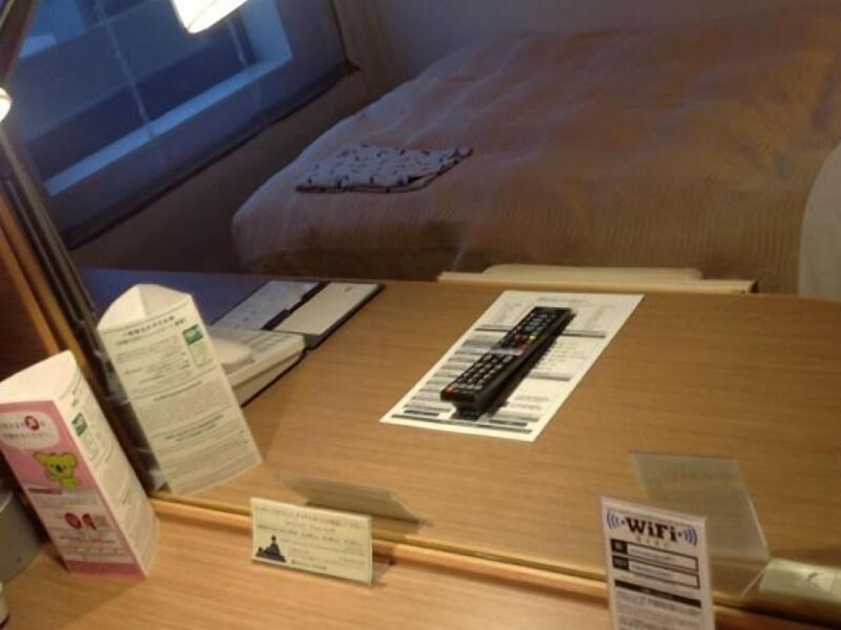 Una camera d'albergo con un letto, una scrivania con un telecomando, il simbolo del Wi-Fi e un piccolo cartoncino sulla scrivania.