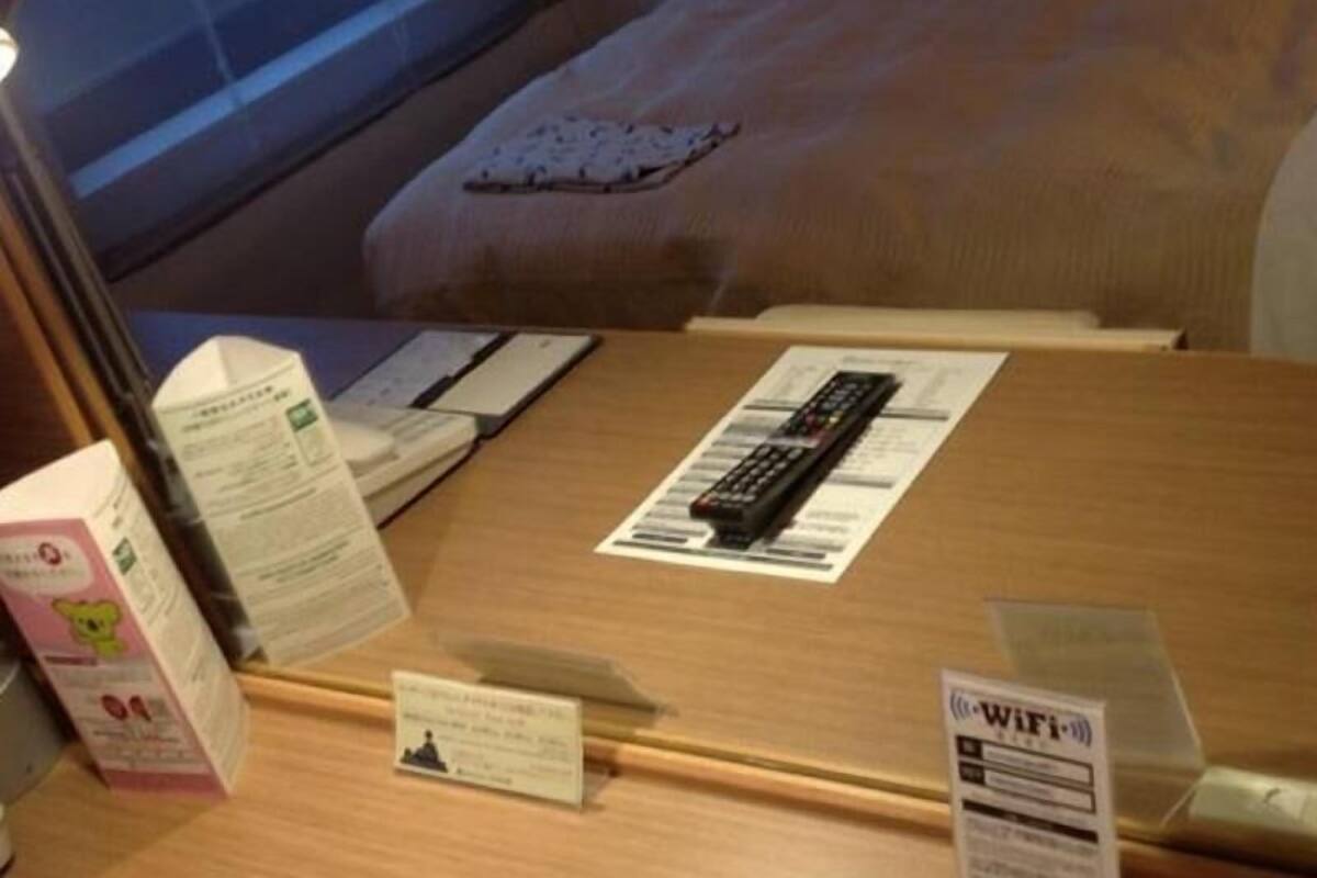 A hotel room with a bed, a desk with a remote control, a Wi-Fi sign, and a small card on the desk.