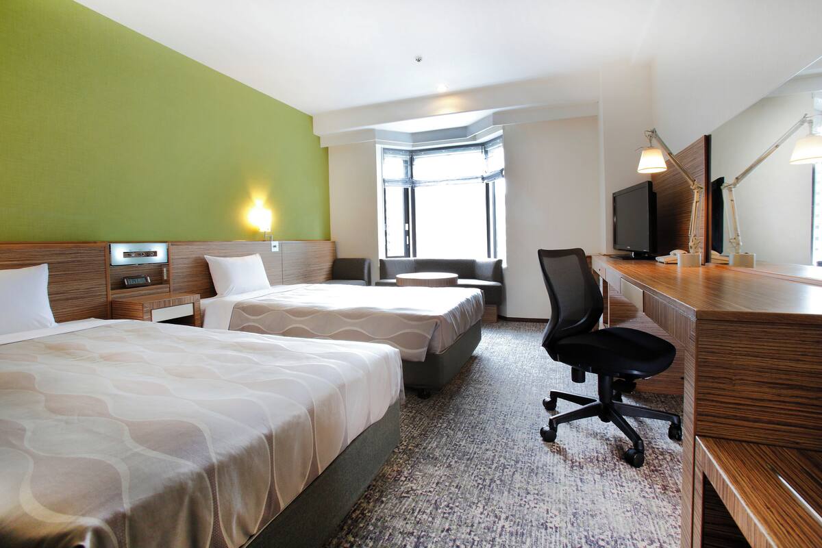 A hotel room with two beds, a desk with a computer, a TV, and a window with a view.