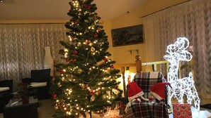 A Christmas tree with lights and ornaments, a plaid chair with a Santa hat, and a reindeer decoration. - Leotel Hotel (Lviv)
